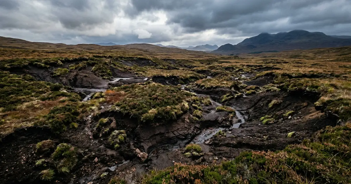 Landscape view of degraded moorland and peatland habitat showing erosion patterns, fragmented vegetation patches, and atmospheric sky over Scottish upland terrain